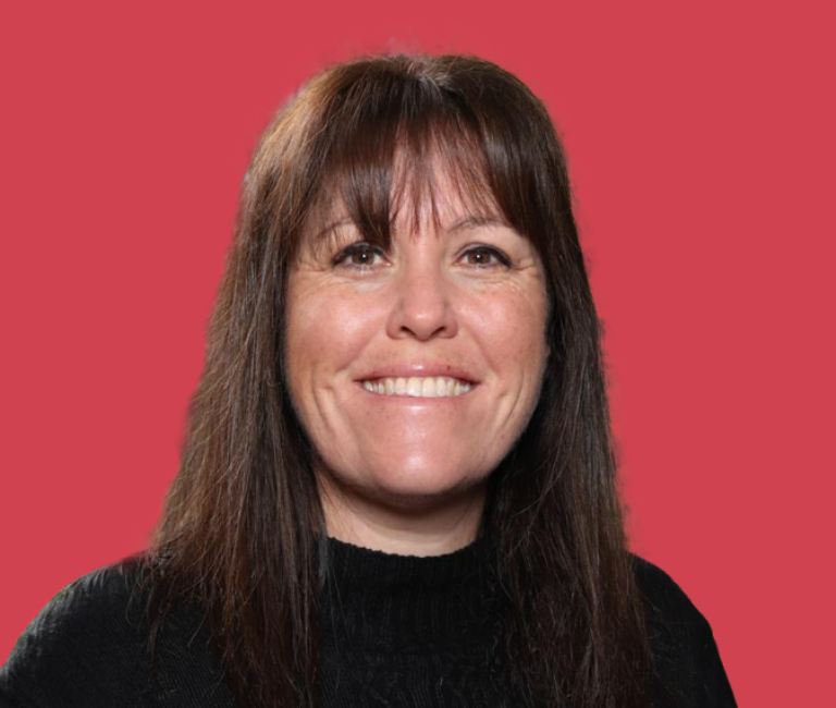 Priscilla Caragh - Headshot of a middle-aged woman with long, brown hair, wearing a black top and smiling.