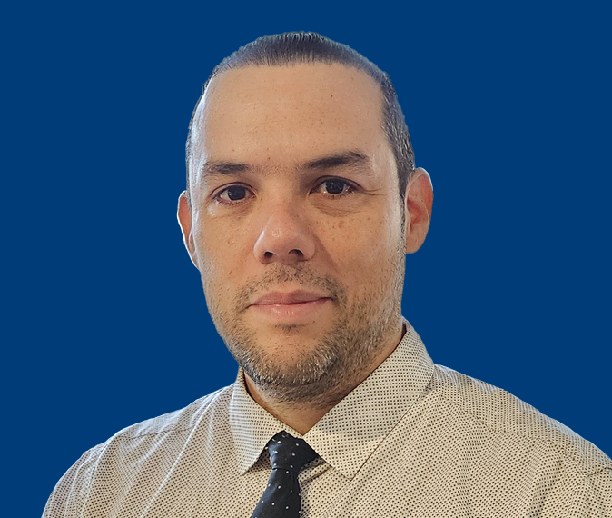 Hector Peralta - Headshot of a young man with dark, short hair, wearing a shirt and tie and looking serious.