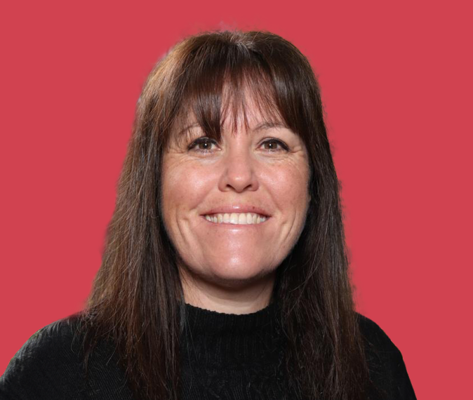 Priscilla Caragh - Headshot of a middle-aged woman with long, brown hair, wearing a black top and smiling.