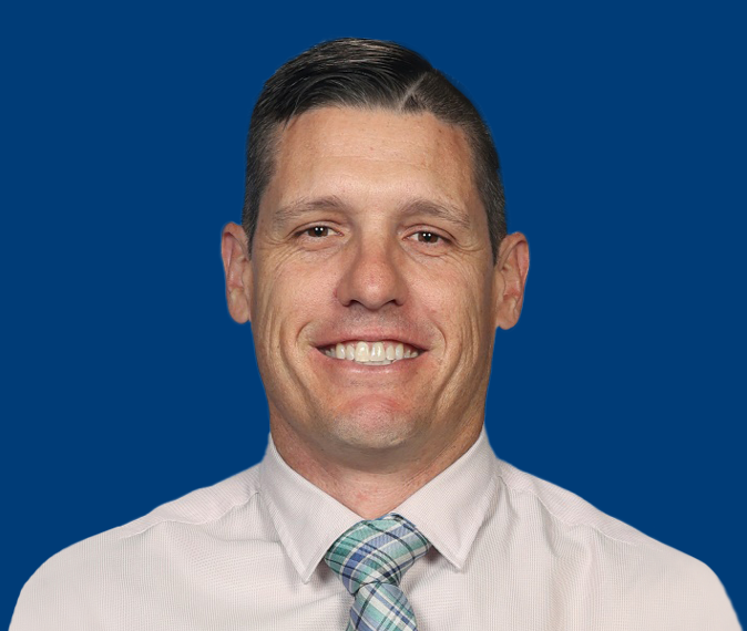 Craig Hubbard – headshot of a man with short brown hair, wearing a collared shirt and green and blue checked tie looking at camera smiling.